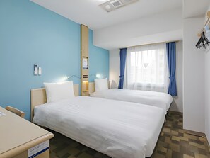 Ein Hotelzimmer mit zwei Betten, einem Schreibtisch, einem Spiegel und einem Fenster mit Vorhängen.