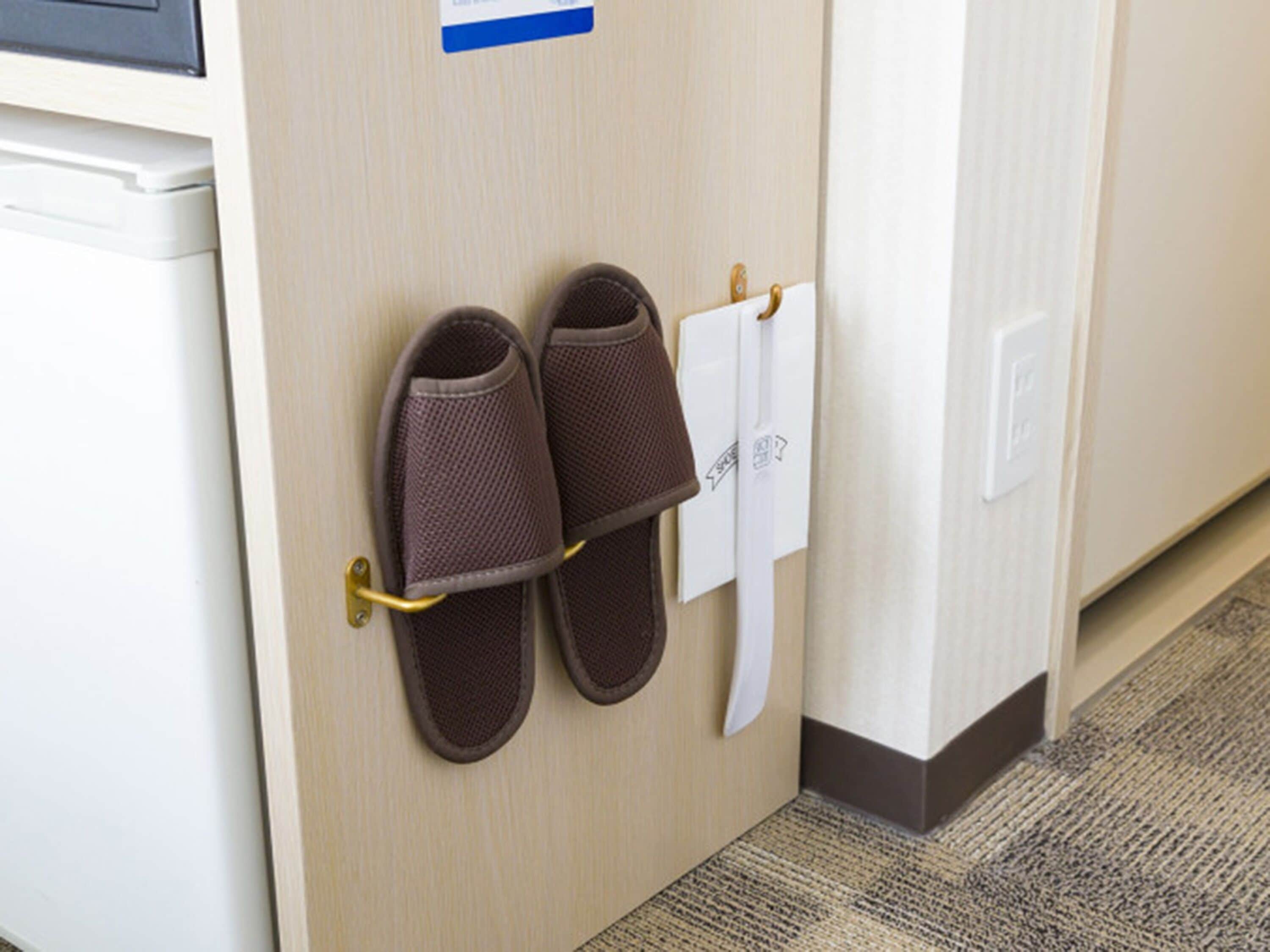Un par de pantuflas marrones colgadas en un gancho metálico adherido a una puerta de madera.