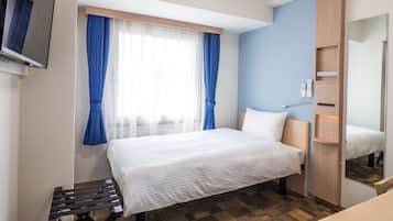 A hotel room with a bed, a small table, a mirror, and a wardrobe.