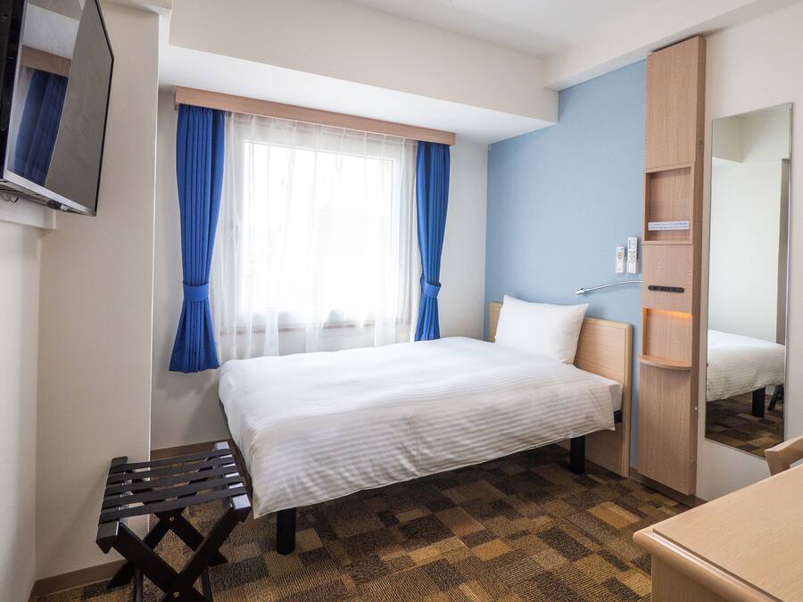 A hotel room with a bed, a small table, a mirror, and a wardrobe.