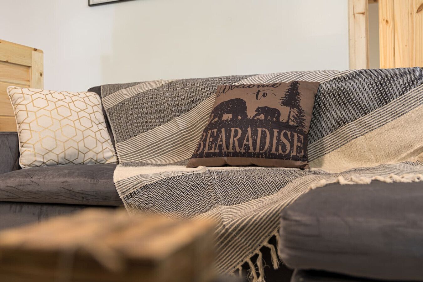 A sofa with patterned cushions and a pillow with 'Welcome to BEARADISE' text.