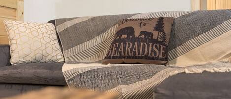 A sofa with patterned cushions and a pillow with 'Welcome to BEARADISE' text.