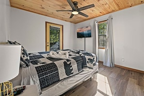 A bedroom with a bed, a ceiling fan, a TV, and a window.