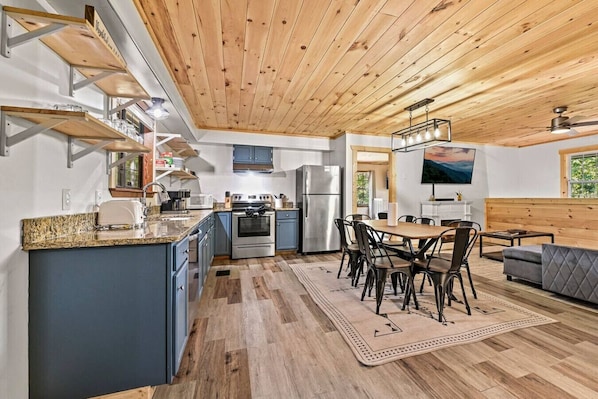 A modern kitchen with granite countertops, a dining area with a wooden table and chairs, and a cozy seating area with a sofa.
