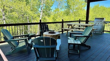 Une terrasse couverte avec des fauteuils Adirondack et un barbecue.