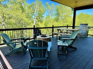 Relax on the deck with Adirondack chairs and picnic tables, surrounded by lush greenery and a grill station.