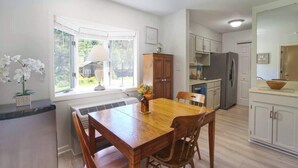 Una cocina con armarios blancos, una mesa de comedor de madera y un refrigerador.