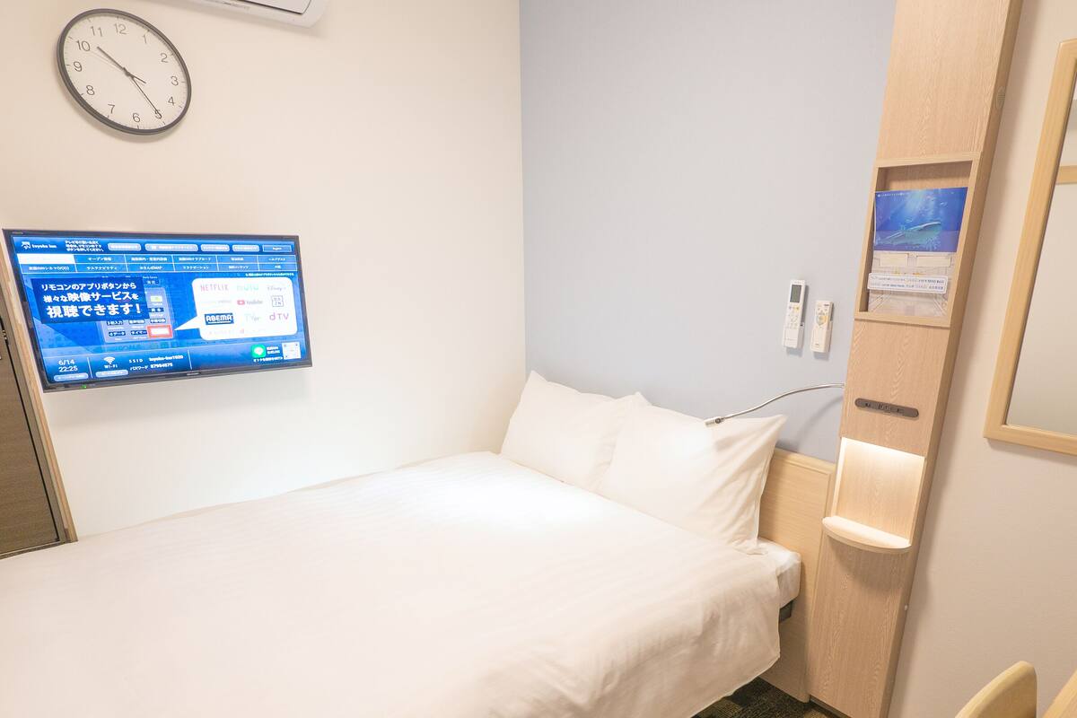 A hotel room with a bed, a clock, a TV displaying a menu, and a wooden cabinet.