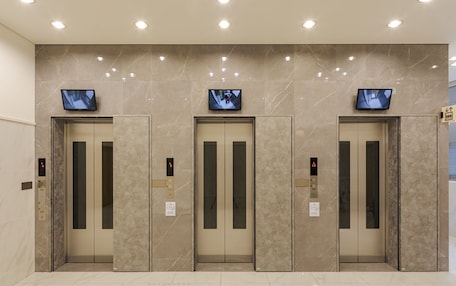 Three elevator doors with digital displays, a marble wall, and a tiled floor.