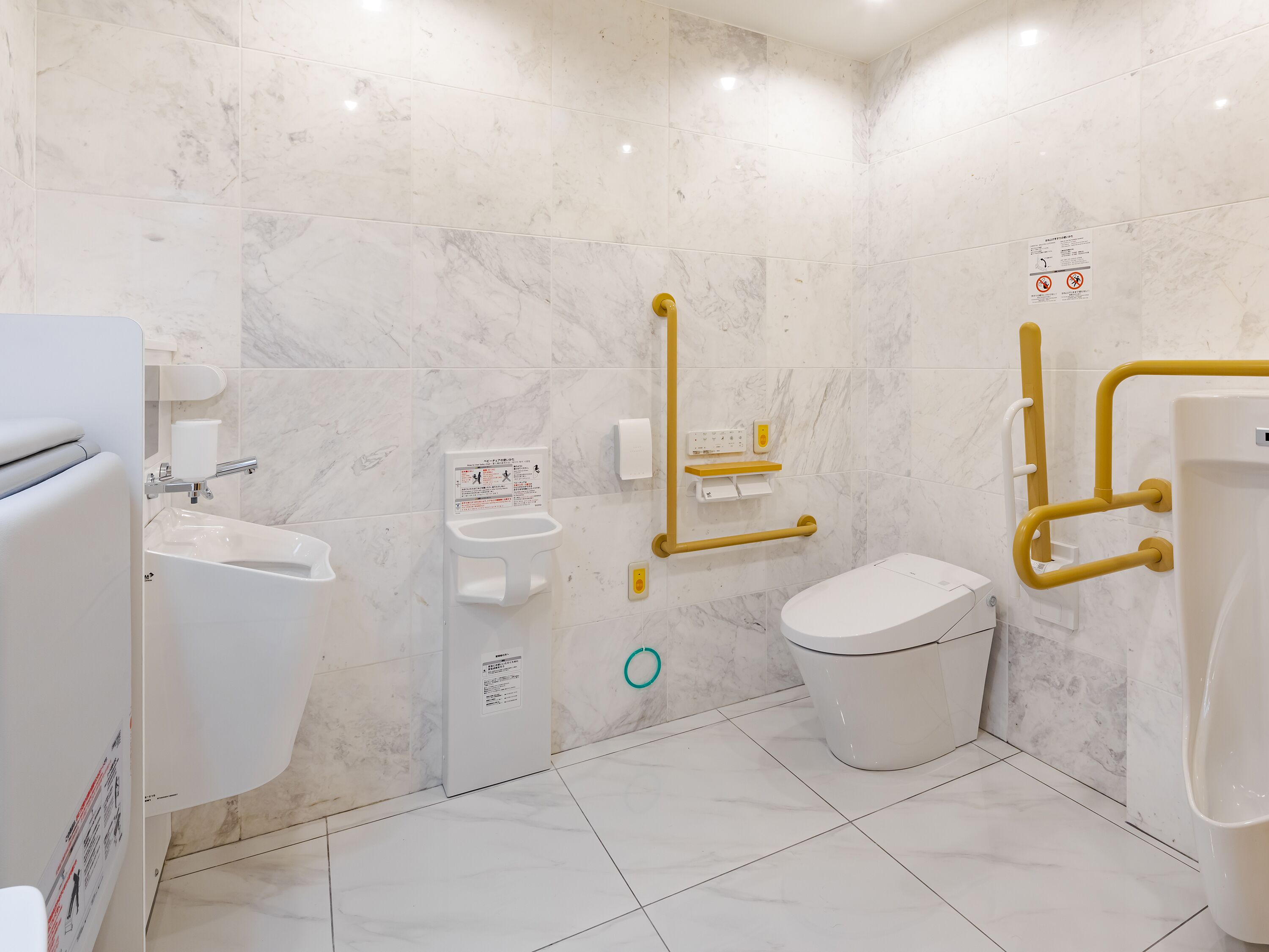 Un baño moderno con inodoro, bidé y lavamanos, equipado con elementos de accesibilidad como barras de apoyo y pasamanos.