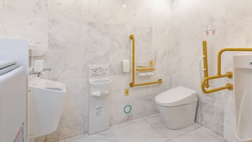 Un baño moderno con inodoro, bidé y lavamanos, equipado con elementos de accesibilidad como barras de apoyo y pasamanos.