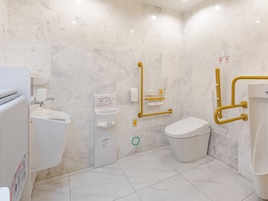 Un baño moderno con inodoro, bidé y lavamanos, equipado con elementos de accesibilidad como barras de apoyo y pasamanos.