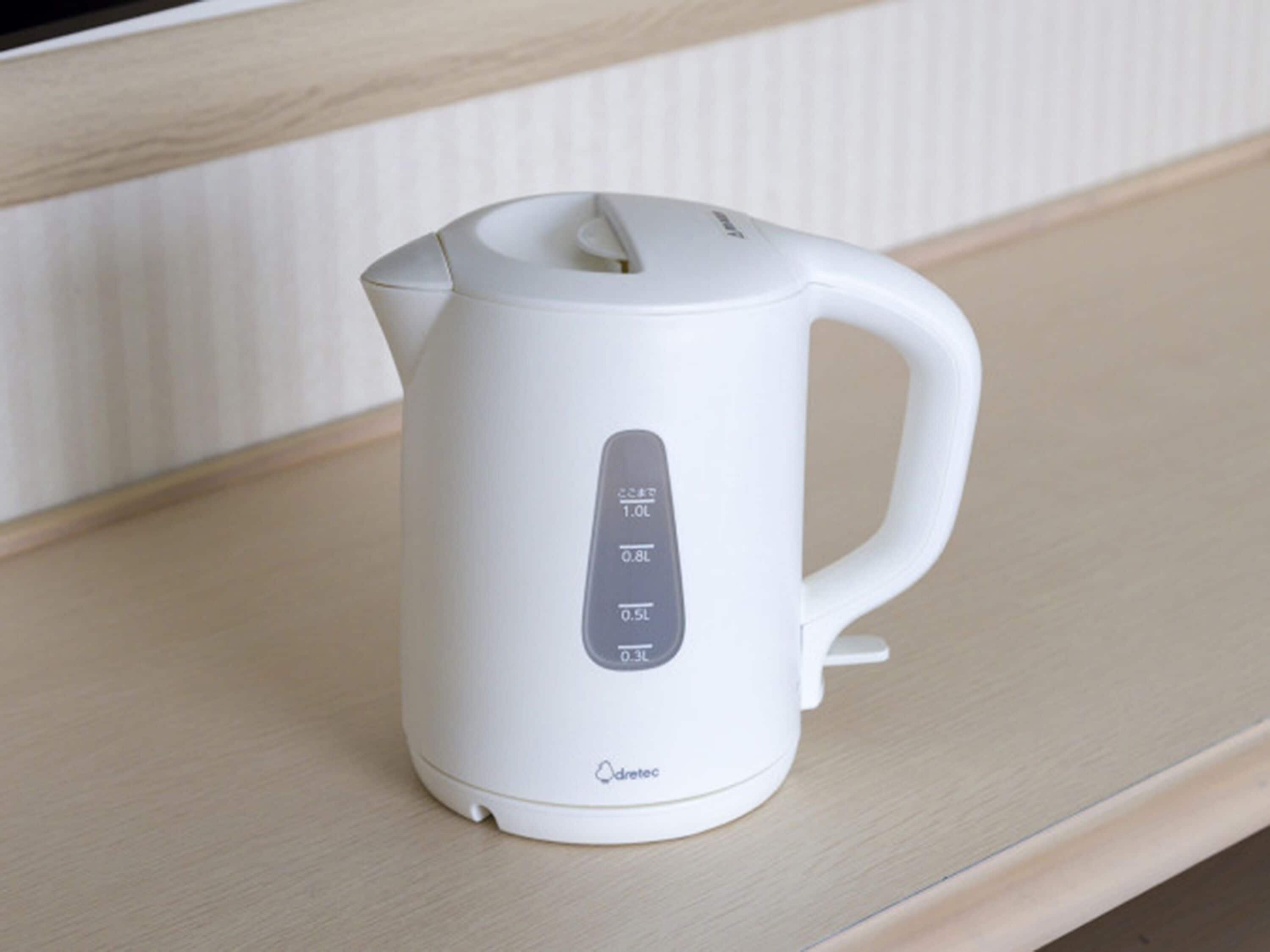 A white electric kettle with measurement markings on its side, placed on a wooden surface.