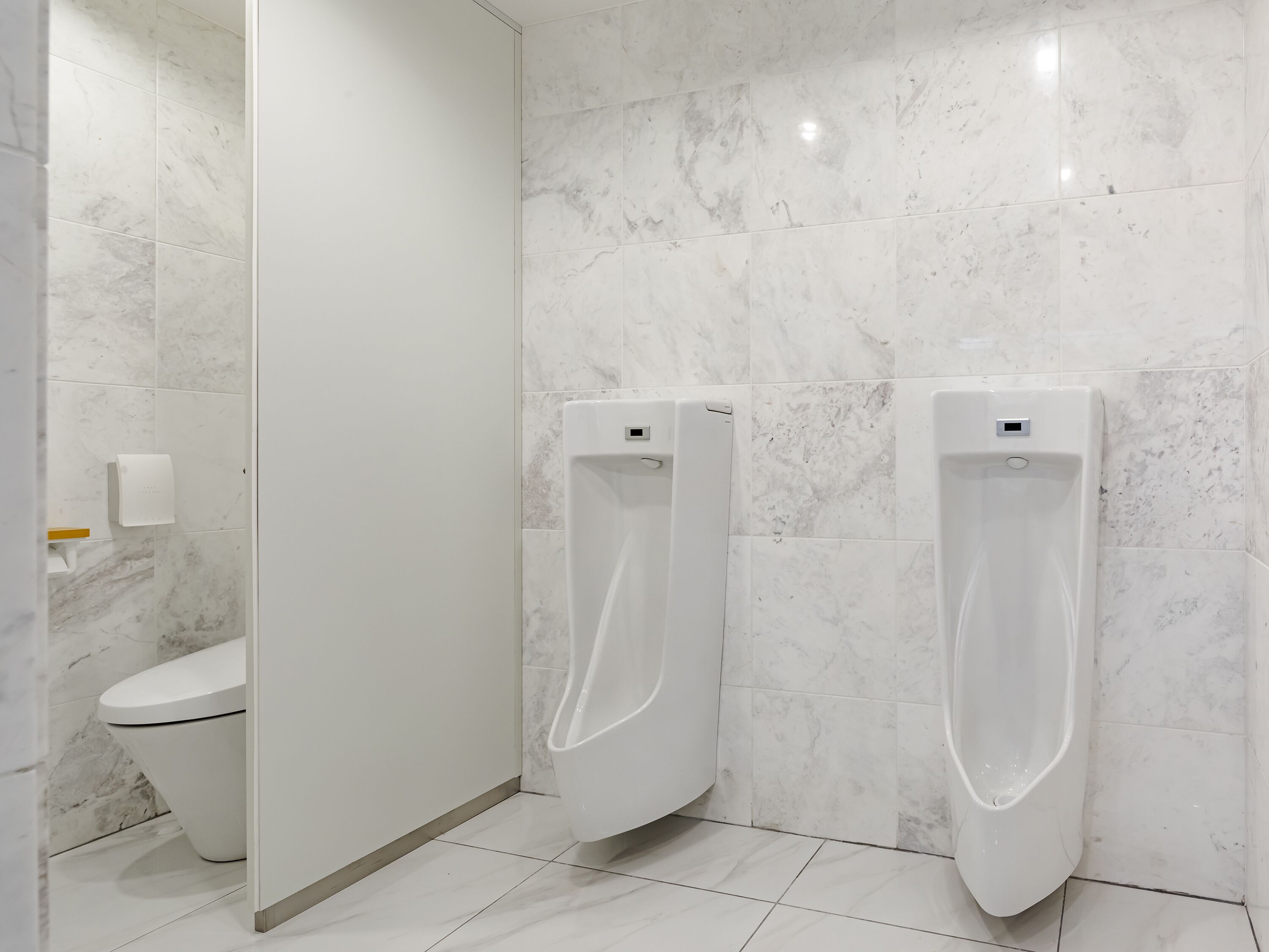 Un baño moderno con dos orinales, un inodoro y un dispensador de toallas de papel.