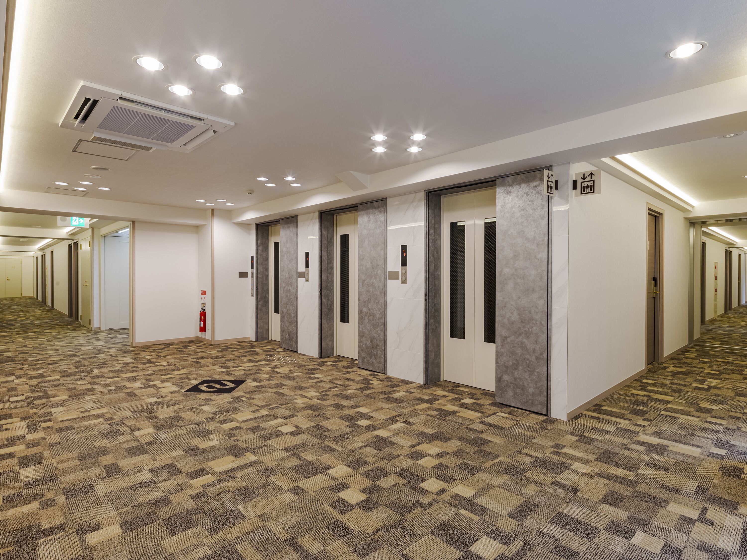 A hotel corridor with a checkered carpet, multiple doors, and a fire extinguisher.