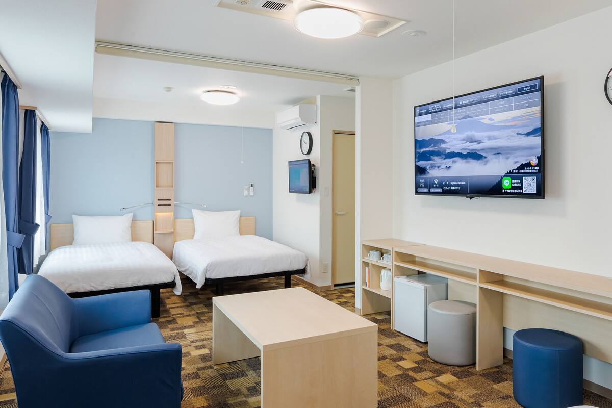 A hotel room with two beds, a desk, a chair, a TV, and a clock on the wall.