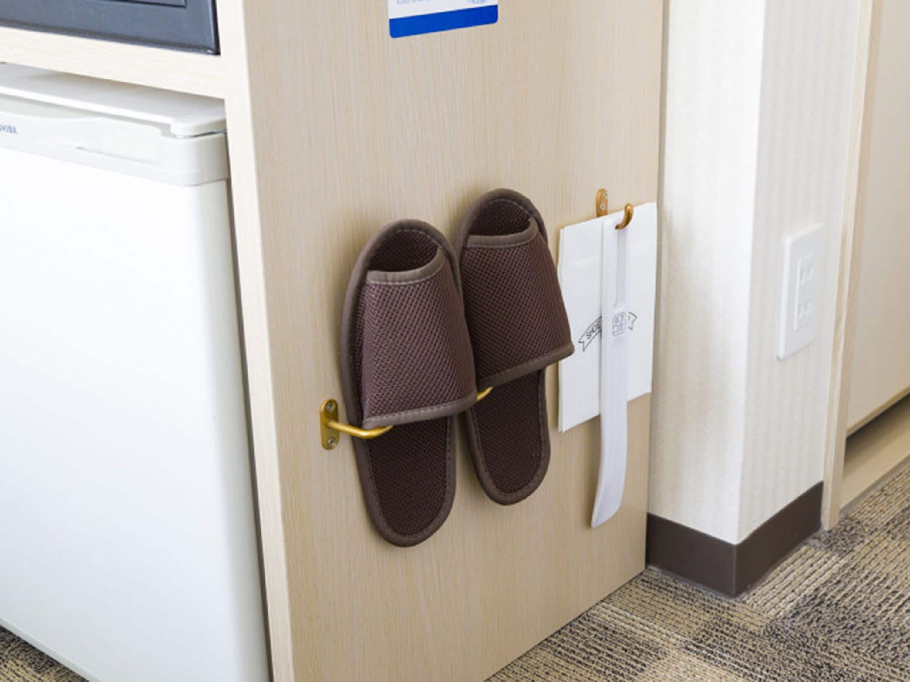 A pair of brown slippers hanging on a metal rack attached to a wooden door.