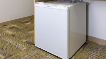 Un refrigerador blanco pequeño en una esquina de una habitación con alfombra a cuadros.