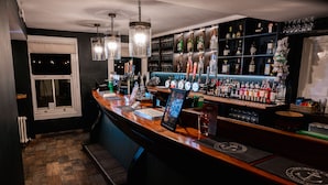A bar area with a wooden counter, multiple liquor bottles, and a variety of glasses. - The Hope & Anchor (Ross-on-Wye)