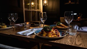 A dimly lit restaurant with a wooden table set for a meal, featuring plates of pasta and a glass of water. - The Hope & Anchor (Ross-on-Wye)