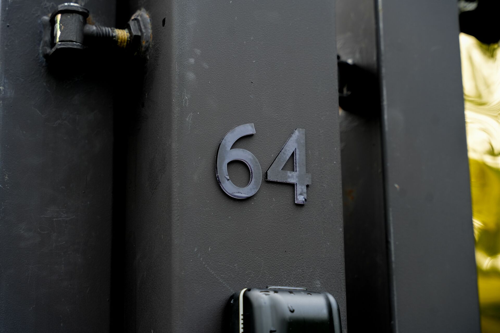 Primer plano del número '64' metálico en una puerta de color oscuro.