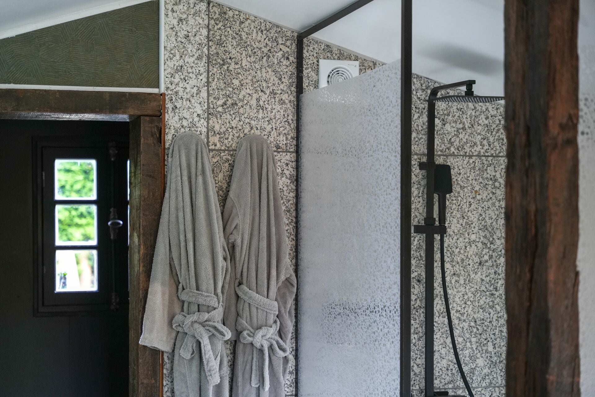 Un baño con ducha, un perchero con dos toallas y una puerta con ventana.