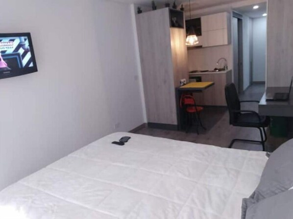 A compact room with a bed, a desk, and a kitchenette.