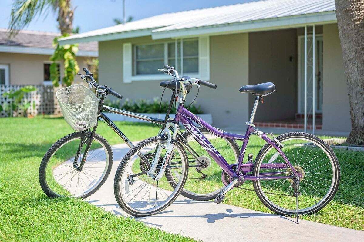 Un vélo violet est garé sur un trottoir, devant une maison dont la porte est blanche et qui possède un petit porche.
