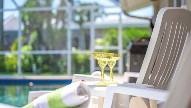 Ein Liegebereich am Pool mit einem Glastisch, zwei goldenen Gläsern und einem weißen Stuhl.