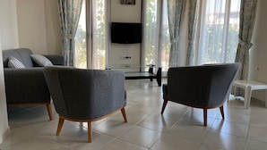 A living room with two grey armchairs, a sofa, a flat-screen TV, and a glass coffee table.