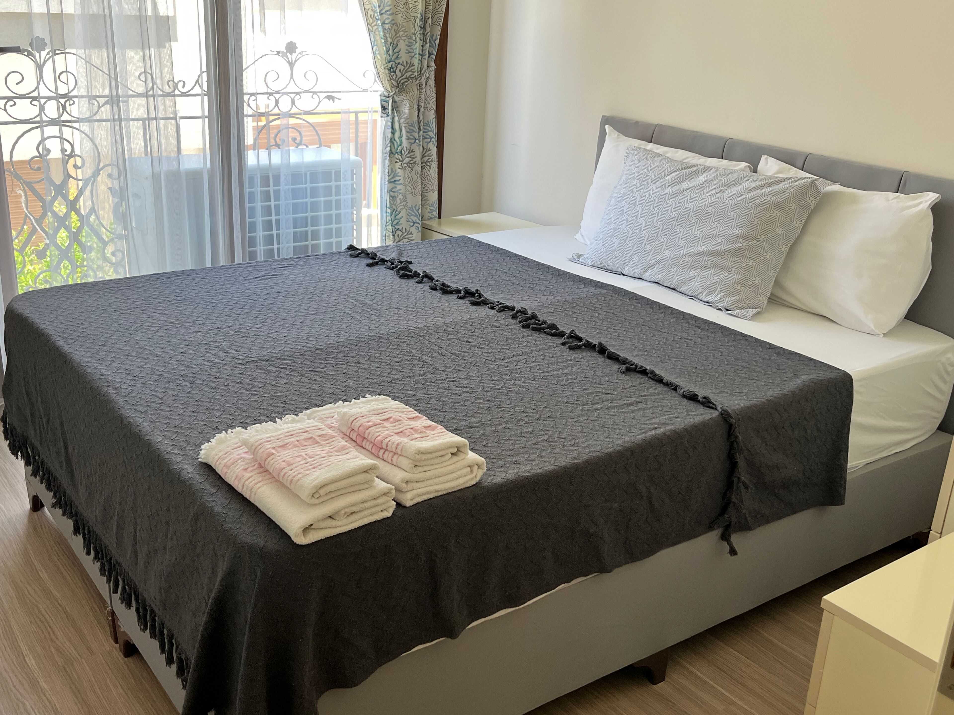 A neatly made bed with a dark blanket, two pillows, and folded towels on the side.