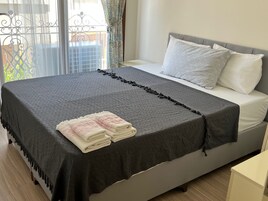 A neatly made bed with a dark blanket, two pillows, and folded towels on the side.
