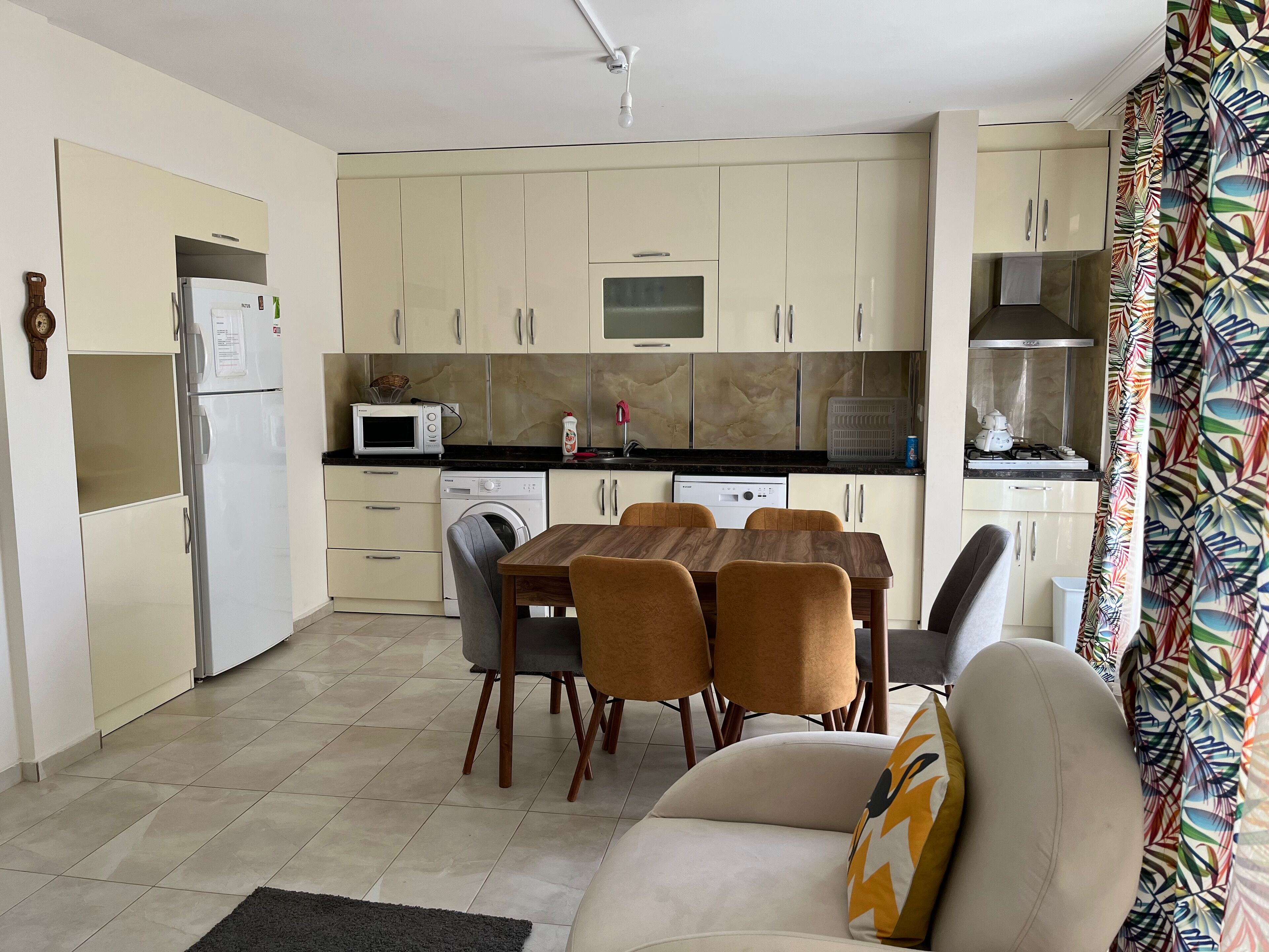 A compact kitchen with a dining area, including a table with chairs, a washing machine, and a microwave.