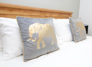 Un letto con due cuscini decorati con motivi di elefanti, una testiera in legno e un oggetto nero sopra la testiera.