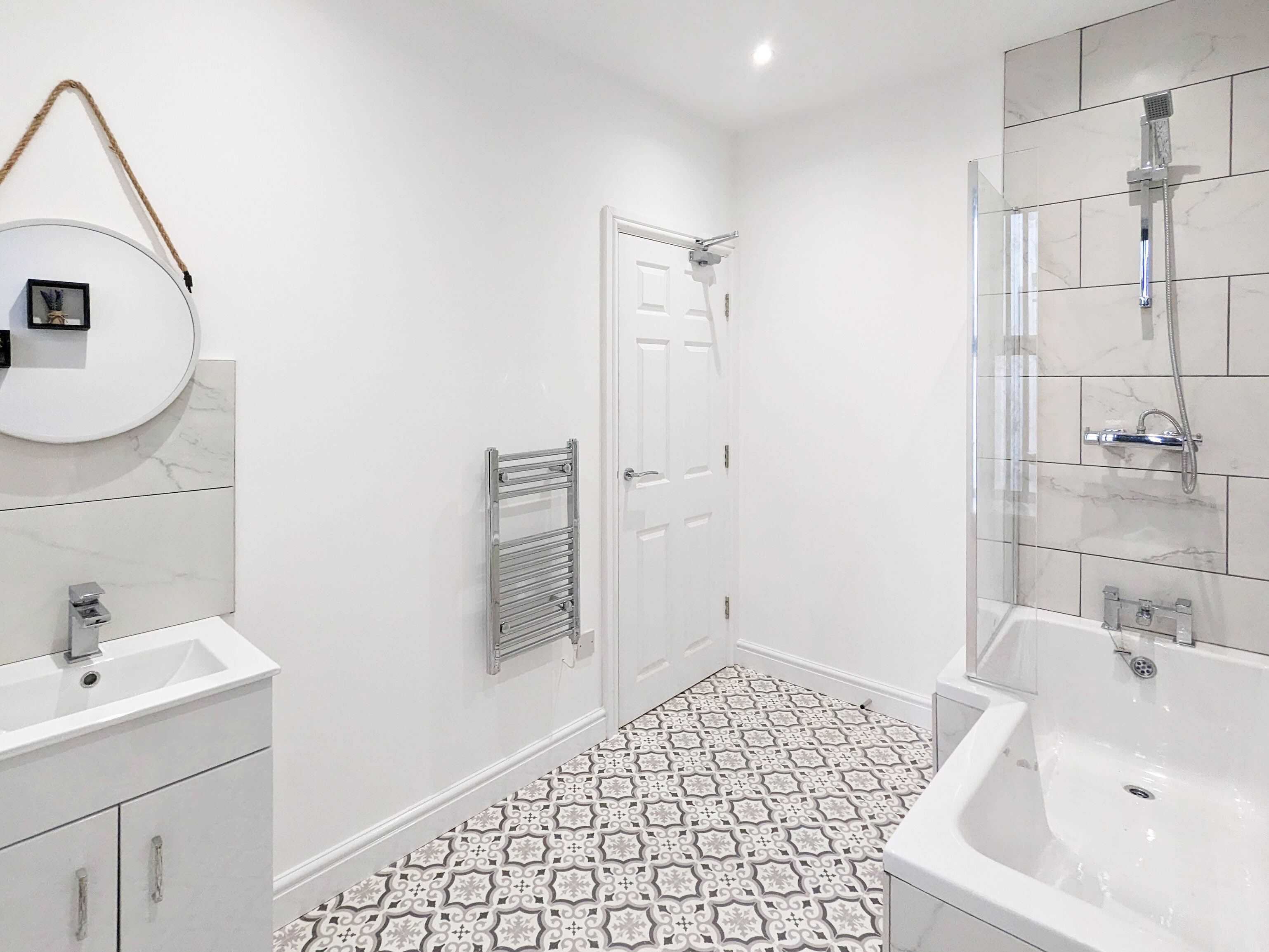 Un bany modern amb un lavabo blanc, un mirall, una dutxa i rajoles de terra amb disseny.