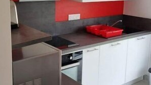 Une cuisine moderne avec des meubles blancs, un mur d’accent rouge et un réfrigérateur en acier inoxydable.