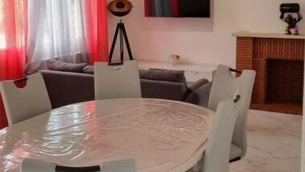 Un salon moderne avec une table ronde, des chaises blanches, un canapé, un téléviseur et une cheminée.