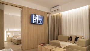 Une chambre d’hôtel moderne avec un mur d’accent en bois, un téléviseur à écran plat, un canapé beige et une petite table d’appoint en bois sur laquelle repose un livre.