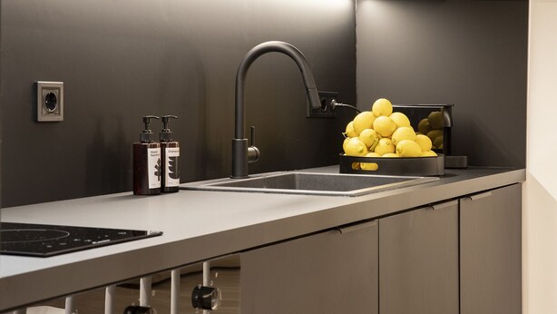 Une cuisine moderne dotée d’un évier en acier inoxydable, d’une hotte intégrée et d’un bol de citrons posé sur le plan de travail.