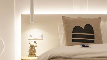 Une chambre moderne au design minimaliste, comprenant un lit recouvert d’une couverture texturée, une table de chevet avec une lampe et un luminaire fixé au mur.