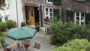 A courtyard with a wooden table and chairs, a green umbrella, and a brick building with a wooden door. - Landhaus in Idyllischer, Ruhiger Lage und Flughafennähe (Ratingen)