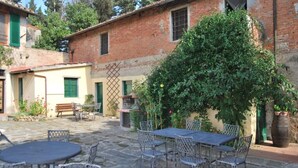 Une cour avec un sol en pierre, des meubles en métal et un grand arbre.