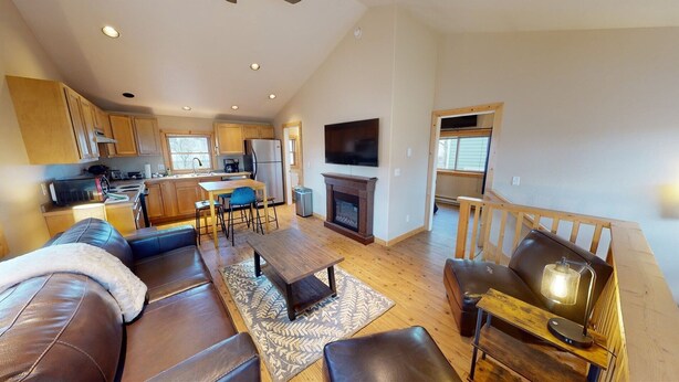 A spacious living area with a sofa, coffee table, and fireplace. There is a kitchen with wooden cabinets and a dining area. - The Mountaineer Apartment - Gunnison (Gunnison)