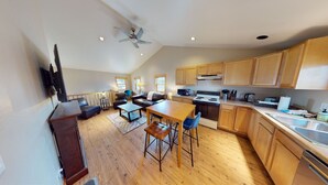 A spacious kitchen with wooden cabinets, a dining area with a table and chairs, a ceiling fan, and a large window providing natural light. - The Mountaineer Apartment - Gunnison (Gunnison)