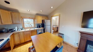 A compact kitchen with wooden cabinets, a stainless steel refrigerator, a coffee maker, and a dining table with chairs. - The Mountaineer Apartment - Gunnison (Gunnison)