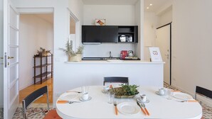 Een eetgedeelte met een witte tafel voor vier personen, een zwarte kast erboven en een kleine potplant op het aanrecht.