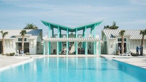Uma área de piscina com uma estrutura central e um design de cobertura único, rodeada por palmeiras e espreguiçadeiras.
