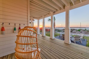 Une terrasse en bois avec une chaise en osier et une table, donnant sur une plage au coucher du soleil.