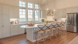 Una cocina moderna con una isla grande, muebles blancos y electrodomésticos de acero inoxidable.