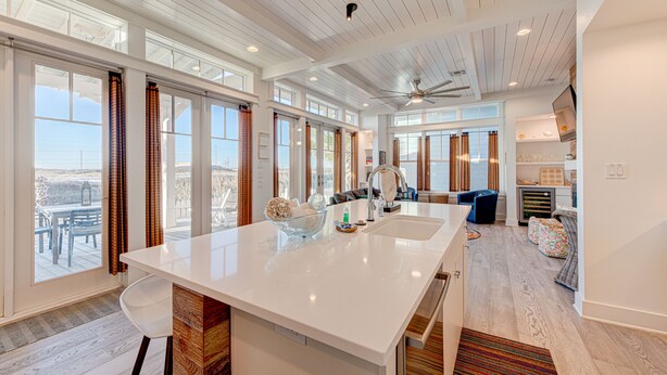 A spacious kitchen with a large island, a ceiling fan, and large windows offering views of the outdoors.